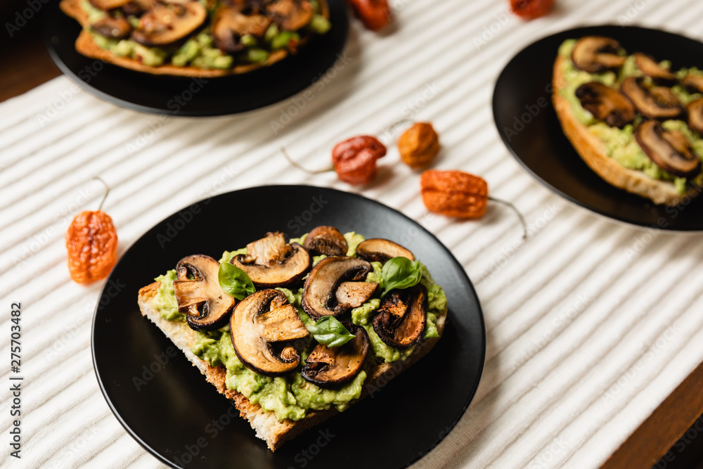 Avocado Toast with Mushrooms On A Black Plate with Light Background Avocado Toast with Mushrooms On A Black Plate with Light Background