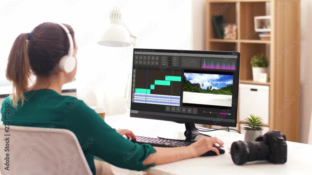 technology, post production and vlog concept - woman in headphones working on travel video in editor program on computer and drinking coffee at home office technology, post production and vlog concept - woman in headphones working on travel video in editor program on computer and drinking coffee at home office