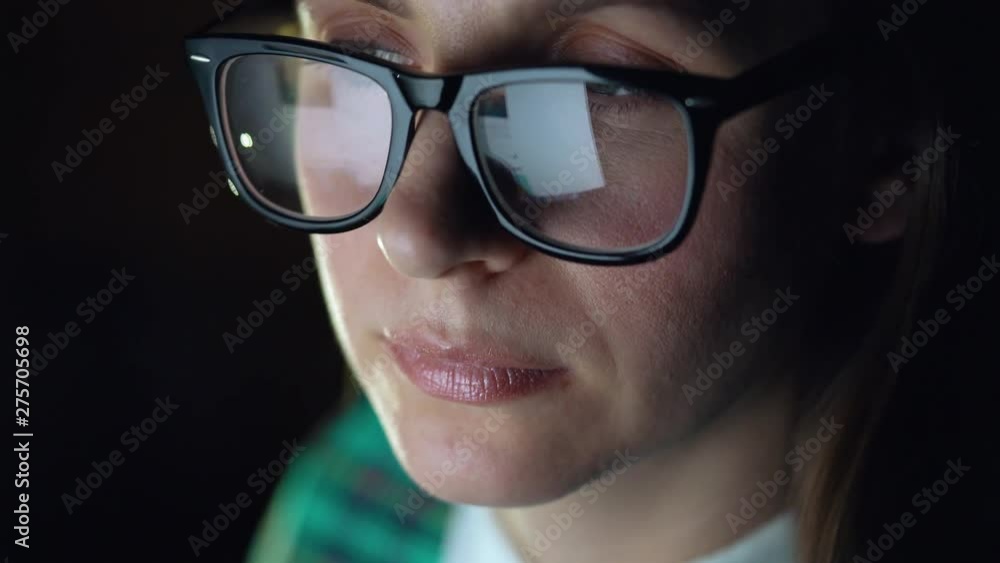 Woman in glasses looking on the monitor and surfing Internet. The monitor screen is reflected in the glasses Woman in glasses looking on the monitor and surfing Internet. The monitor screen is reflected in the glasses