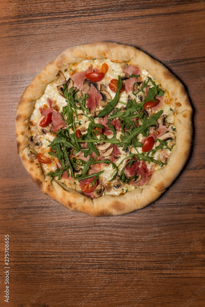 vertical top view of whole pizza with arugula, ham, and tomatoes