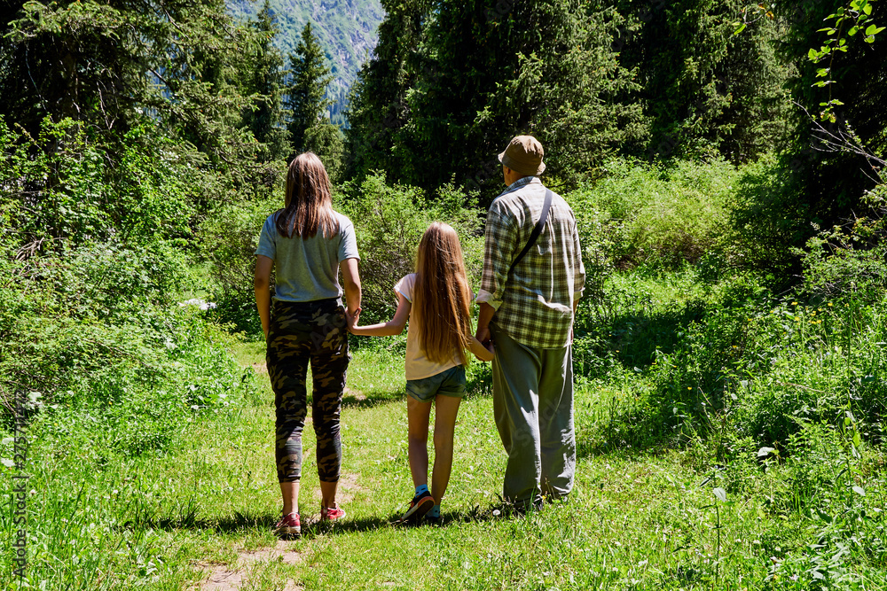 adult man with two children, grandfather walks in a mountain forest with granddaughters, summer sunny day, green background, rest hiking