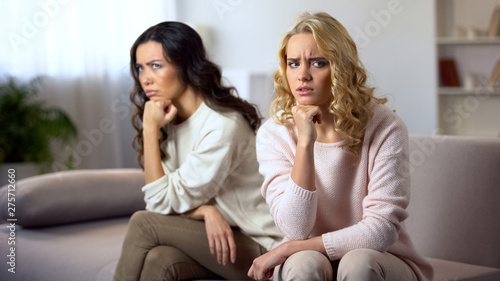 Photography Two offended young woman sitting on sofa, worry about quarrel with best friend