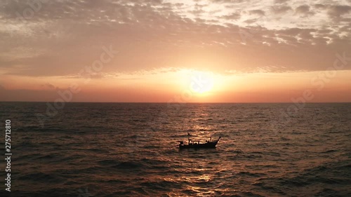 Aerial cinematic drone footage of sea with drifting fishing boat over amazing sunset with cloudy sky photo