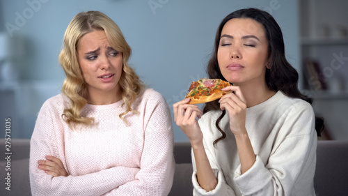 Woman on diet watching her skinny friends enjoying delicious piece of pizza