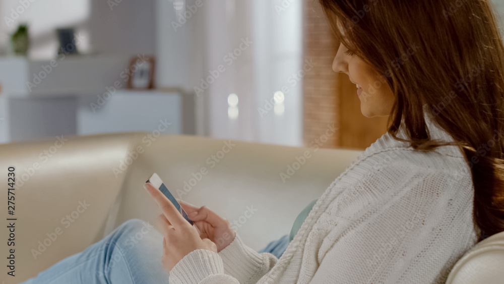 Happy beautiful girl sitting on cozy sofa and making online purchases by phone Happy beautiful girl sitting on cozy sofa and making online purchases by phone