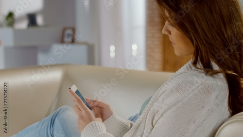 Beautiful girl sitting on comfortable sofa and making online purchases by phone