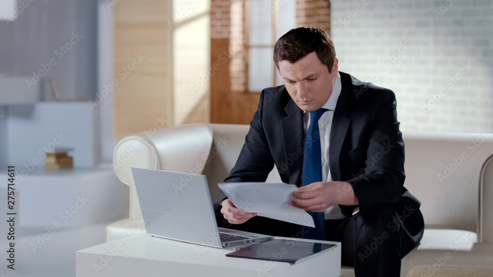 Serious businessman checking company report, working on laptop in modern office Serious businessman checking company report, working on laptop in modern office