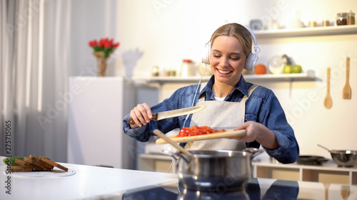 Positive girl listening music and cooking vegetables  healthy low-calorie eating
