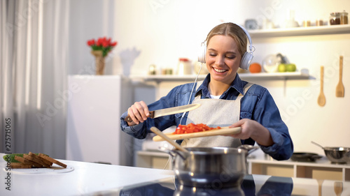 Canvas-taulu Positive girl listening music and cooking vegetables, healthy low-calorie eating