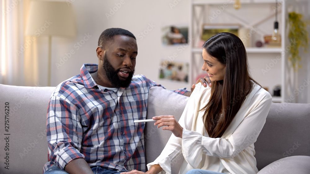 Woman showing pregnancy test to happy Afro-American boyfriend, positive result Woman showing pregnancy test to happy Afro-American boyfriend, positive result