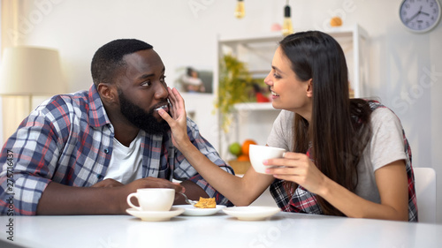 Nice mixed-race couple eating dessert, woman wiping cream from boyfriend lips