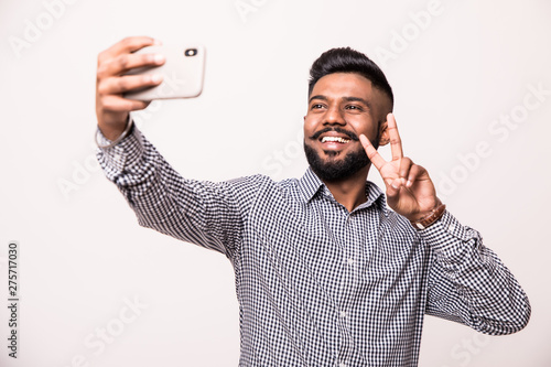 Canvas Print Young indian young man with beard and mustache taking selfie using smartphone ma