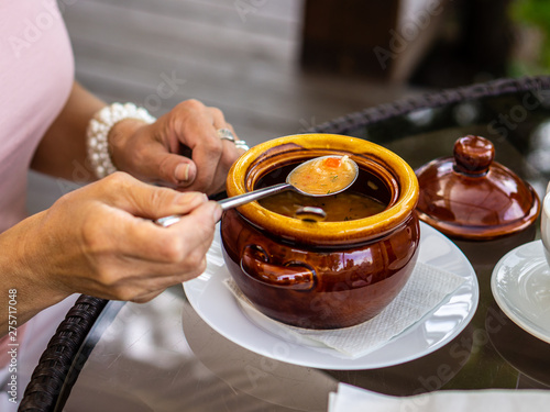 Mature woman eating soup in a brown pot