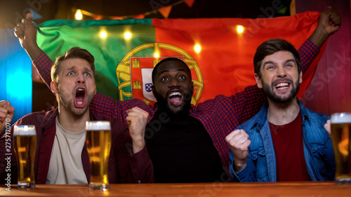 Cheerful portuguese multiracial men celebrating soccer team victory, waving flag