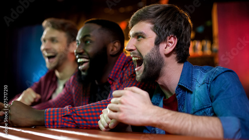 Cheerful multiracial friends screaming, celebrating sports team victory in bar © motortion