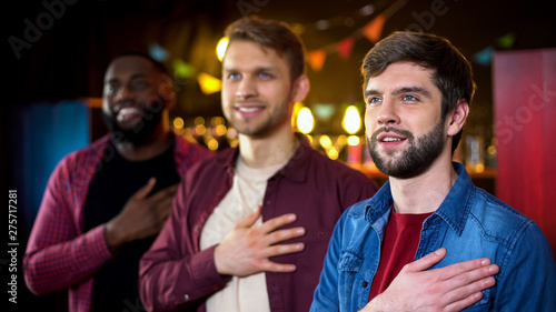 Foto Multiethnic friends listening to anthem before soccer match, results time in pub
