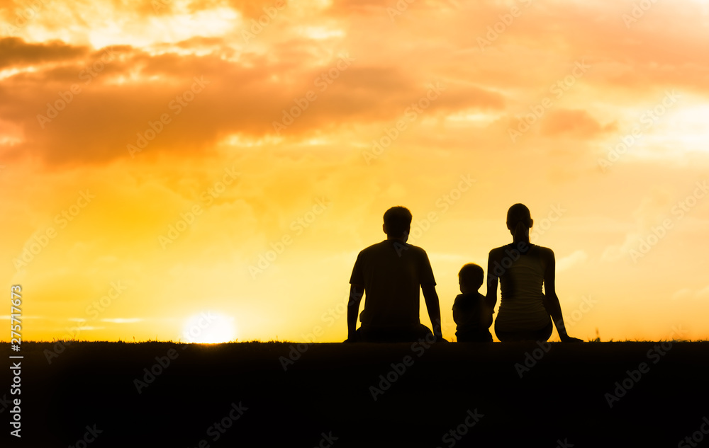 Family of three sitting together at sunset. 