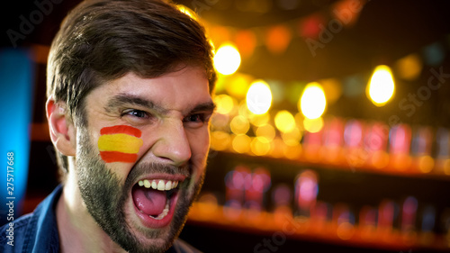 Spanish football fan with flag on cheek cheering for team winning tournament