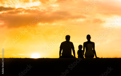 Family of three sitting together at sunset. 