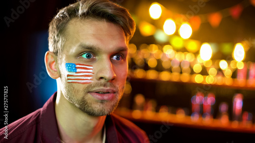 Anxious man with american flag on cheek nervously watching tv, elections results photo