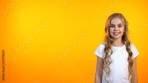 Friendly girl looking to cam and smiling isolated on orange background, template