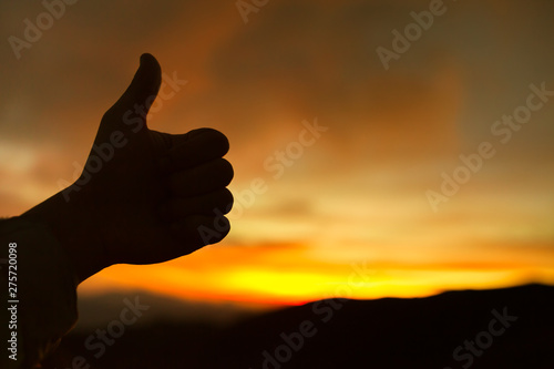 Hand with thumbs up on sunset background. 