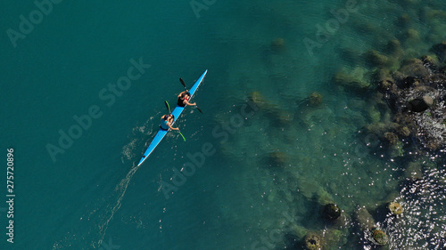 Aerial drone top view of sport canoe operated by 2 young fit athletes in tropical lake with clear water