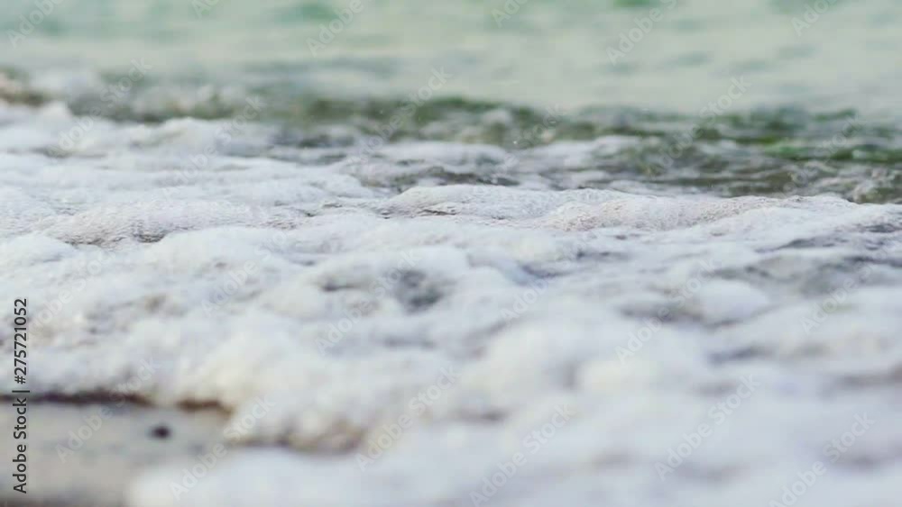 Flowing sea water on the beach with white foam in the evening. The edge of the ocean with foam waves hitting into the shoreline background. Close-up. Flowing sea water on the beach with white foam in the evening. The edge of the ocean with foam waves hitting into the shoreline background. Close-up.