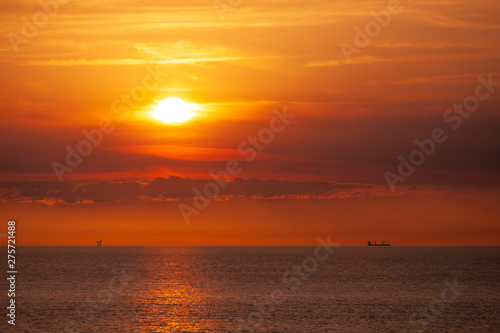 An oil platform and a cargo ship in the sea in the distance on the horizon in the sunset.
