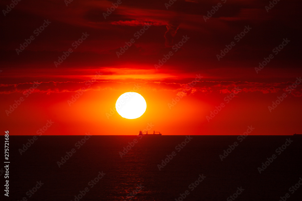 Cargo ship on the sea in sunset with cloud formations in red light Cargo ship on the sea in sunset with cloud formations in red light