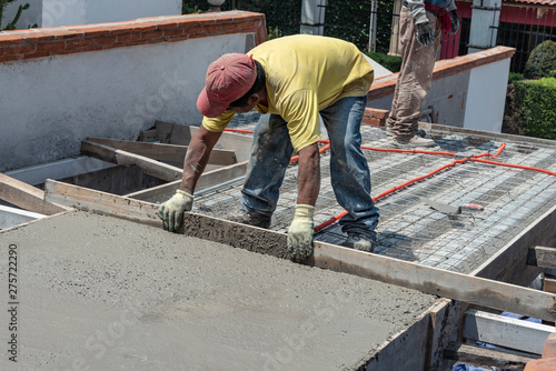 Worker levels a floor cement mortar. Using a straight wooden board to level a rooftop
