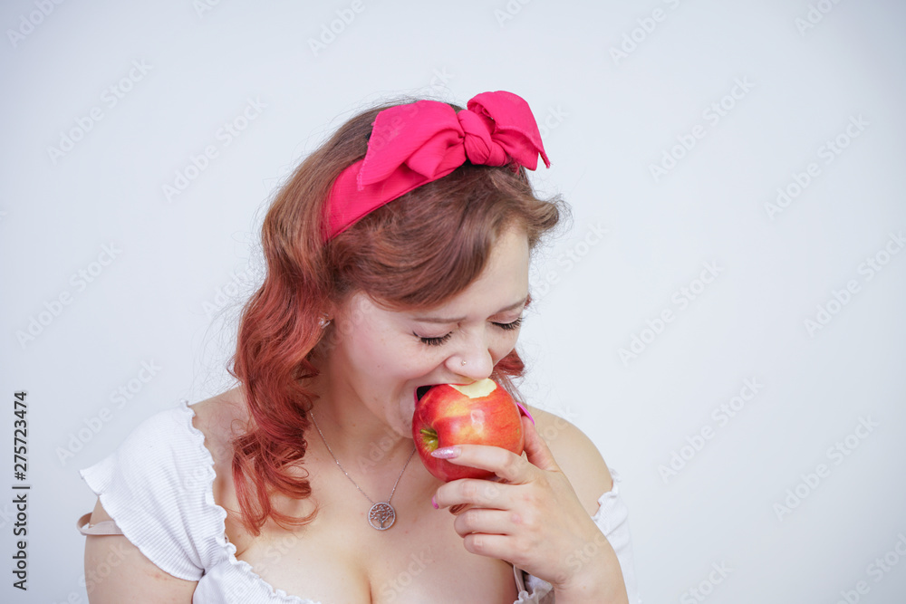 pretty pin up caucasian young girl happy posing with red apples. cute vintage lady in retro dress having fun with fruits on white background alone. vegetarian funny female loves good food and vitamins
