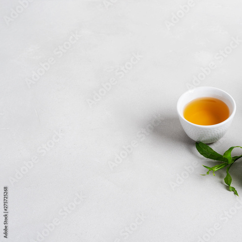 White cup of tea surrounded with fresh tea leaves on concrete background with copy space.