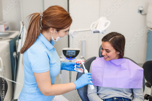 Friendly dentist shows to the patient how to properly brush his teeth with an electric brush. Teeth care and hygiene concept.