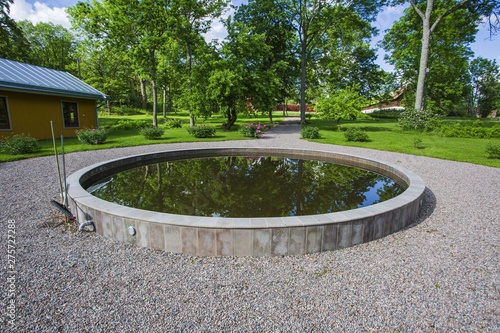 Beautiful view of round decorative outdoor fish pond on green trees background. Outdoor landscape design concept.
