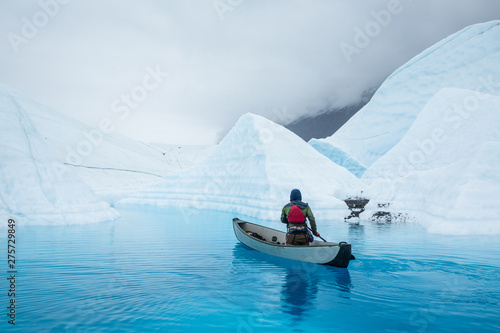 Ice climber in inflatable canoe paddling across a glacier lake on top of the Matanuska Glacier in Alaska.