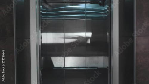 The elevator doors open. Opening the door is an elevator. Metal doors smoothly open and close. Silver and beige new elevator in 4k video.