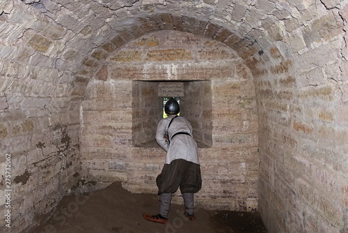 A boy in a historical Viking costume looks into a loophole of the fortress inside the fortress wall © Sergey