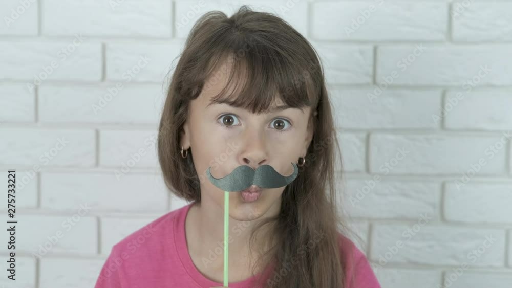 Portrait of a child with a mustache. Mustache day. A cheerful little girl grimaces in a false mustache. Portrait of a child with a mustache. Mustache day. A cheerful little girl grimaces in a false mustache.
