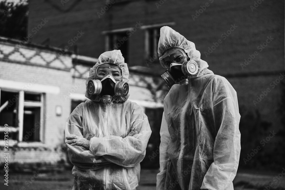 Two scientists put on a respirator and a radiation protective suit. Stern look into the camera from the abandoned territory. Care about ecology in black and white photo mystical horror movie.