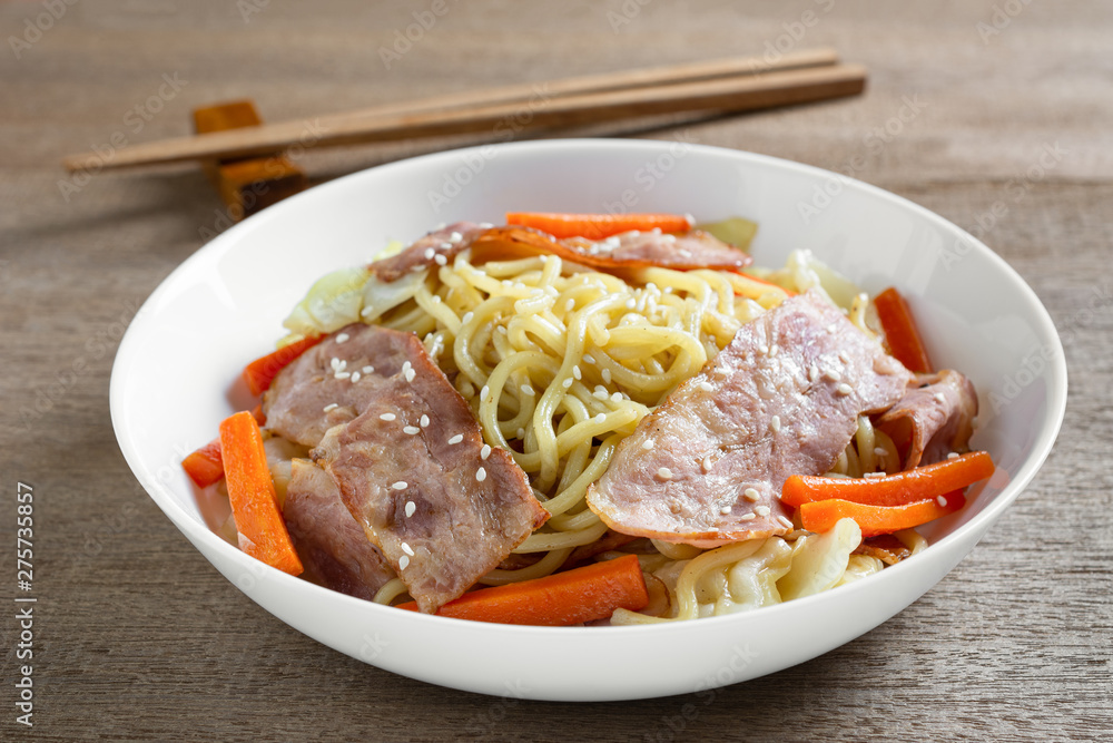 close up of stir fried japanese noodles with bacon and vegetables in a ceramic plate. asian homemade style food concept.