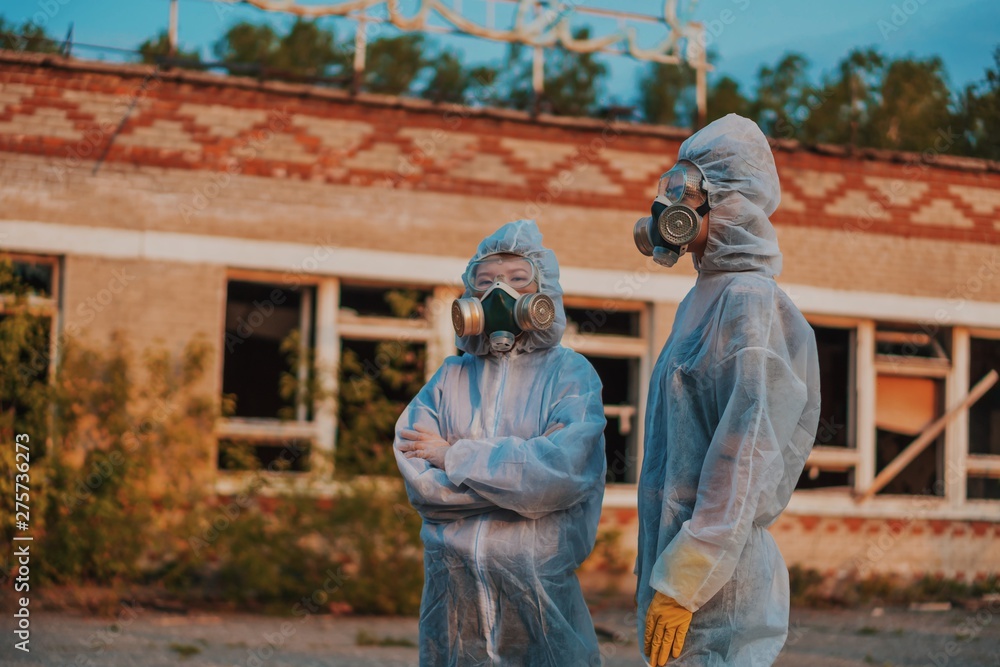 Two scientists put on a respirator and a radiation protective suit. Stern look into the camera from the abandoned territory. Care about ecology in bright saturated photos. Two scientists put on a respirator and a radiation protective suit. Stern look into the camera from the abandoned territory. Care about ecology in bright saturated photos.