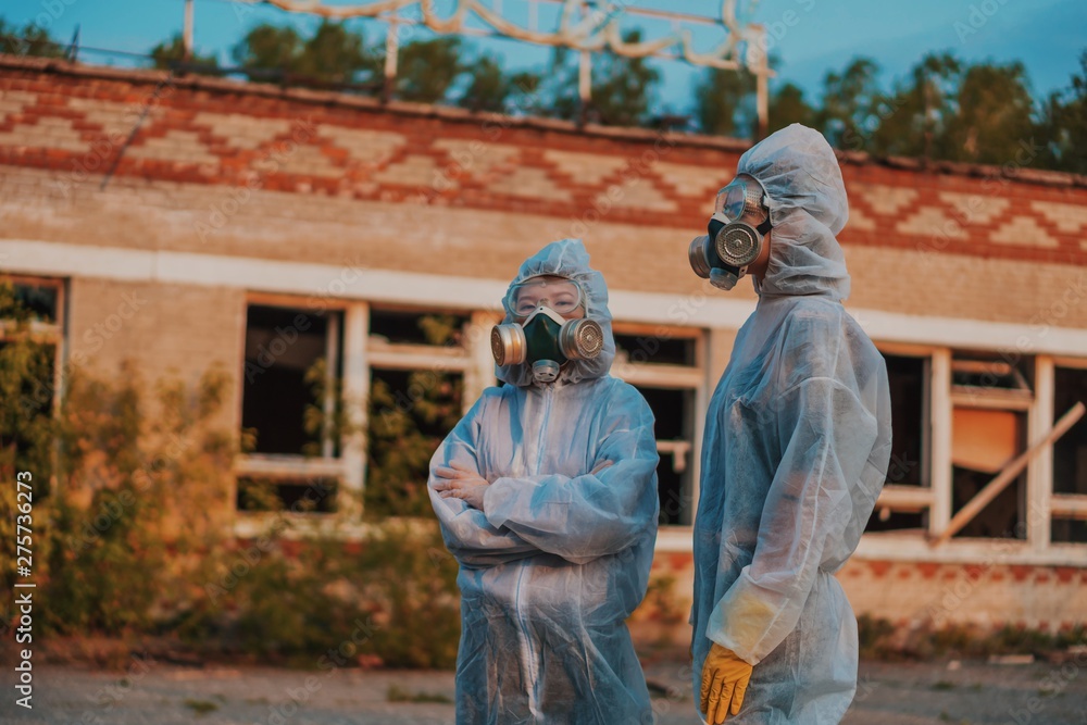 Two scientists put on a respirator and a radiation protective suit. Stern look into the camera from the abandoned territory. Care about ecology in bright saturated photos.