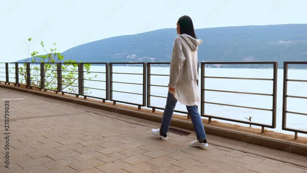 Beautiful Brunette In Casual Clothes Walking On Bridge Along River. Back View. Lonely Timespending Concept. Beautiful Brunette In Casual Clothes Walking On Bridge Along River. Back View. Lonely Timespending Concept.