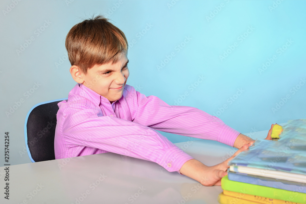 Lazy and stupid teenager does not want to learn and pushes textbooks from himself, sitting at his desk.