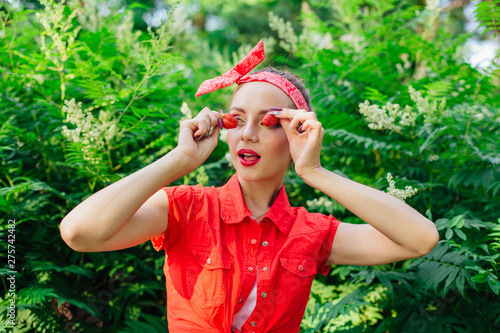 Beautiful young pin up girl with bright make up holding fresh natural strawberry near her eyes.