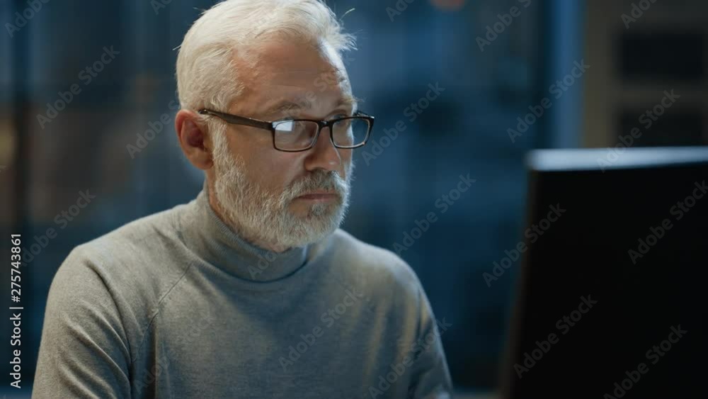 Portrait of the Handsome and Successful Middle Aged Bearded Businessman Working at His Desk Using Laptop Computer. Smiles at Camera. Working at Night from Cozy Home Office / Studio with Window Portrait of the Handsome and Successful Middle Aged Bearded Businessman Working at His Desk Using Laptop Computer. Smiles at Camera. Working at Night from Cozy Home Office / Studio with Window