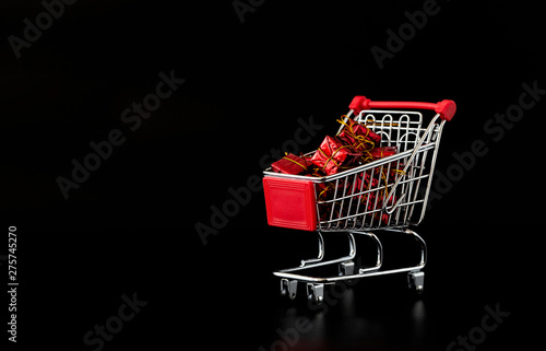 Shopping cart full of gifts. Shopping cart on black background. Minimalist style. Creative design. Copy space. Sale, discount, shopaholism concept. 