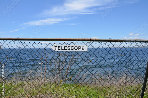 white telescope sign on metal fence and ocean