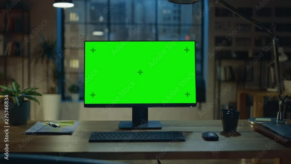 Desktop Computer with Mock-up Green Screen Standing on the Wooden Desk in the Modern Creative Office. In the Background Warm Evening Lighting and Open Space Studio with City Window View. Zoom Out Shot Desktop Computer with Mock-up Green Screen Standing on the Wooden Desk in the Modern Creative Office. In the Background Warm Evening Lighting and Open Space Studio with City Window View. Zoom Out Shot